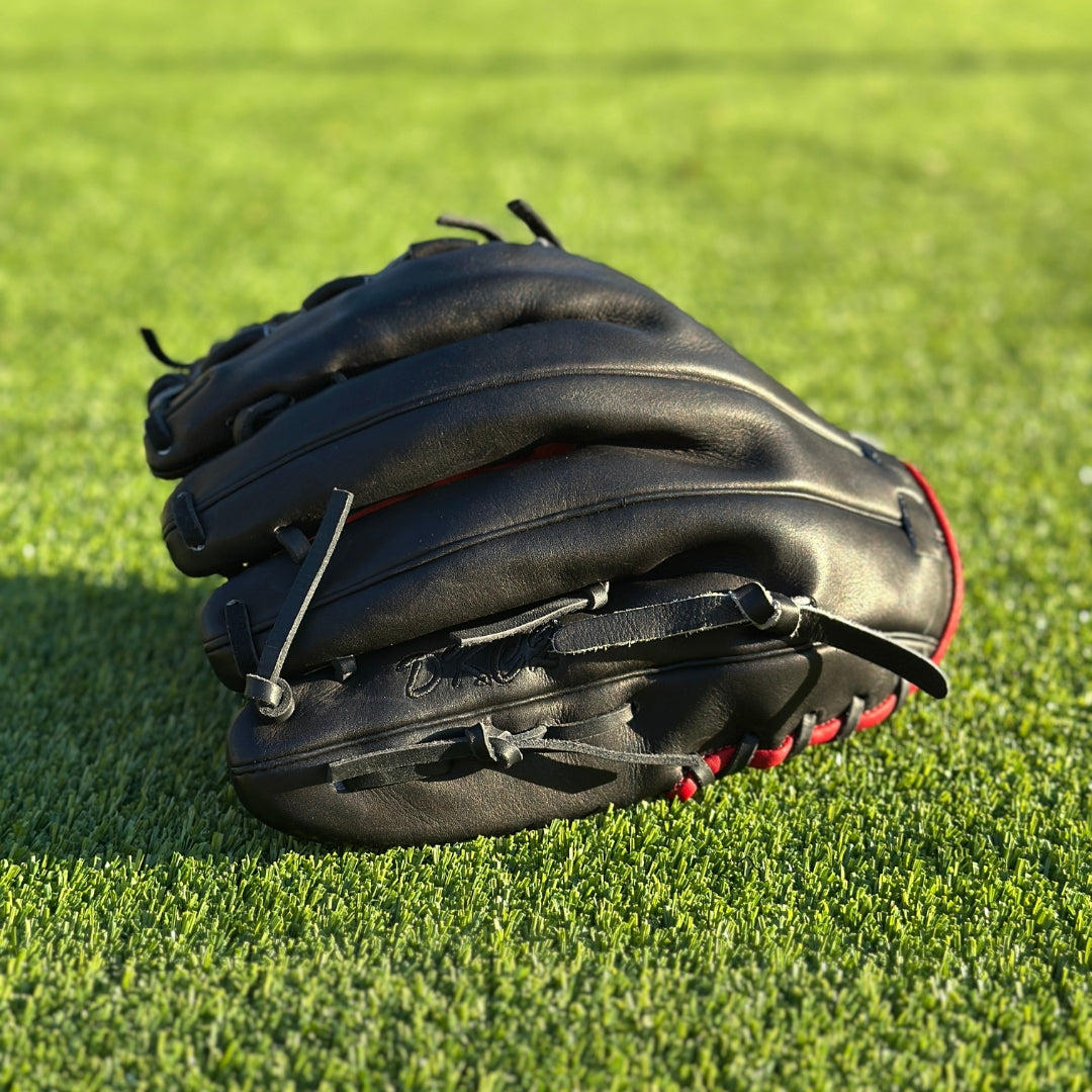 All black with red accent closed back semi-custom baseball glove. The Phantom, set on a turf baseball field