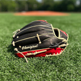 A close-up image of a red and black baseball glove resting on a grassy field. The glove is positioned with the palm facing down, showcasing its intricate blonde lacing, padded leather design, and the hashtag #beoriginal on the pinky. In the background, there is a blurred view of a baseball diamond, indicating that the setting is likely a sports field. The focus on the glove against the soft-focus backdrop highlights its details and suggests its readiness for use in a game.